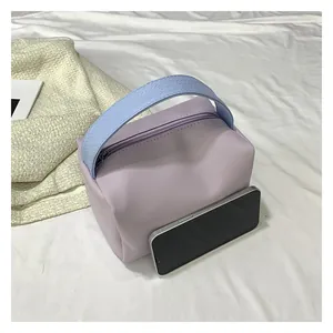 Detail view of small lavender crossbody bag with blue handle shown next to a smartphone