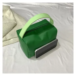 Close-up of green leather handbag showing woven handle and scale compared to a smartphone
