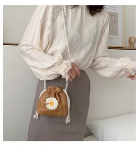 Detail of woven straw bucket bag featuring a white daisy applique and drawstring closure