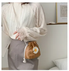 Detail of hand-woven straw bucket bag with white daisy applique and drawstring closure