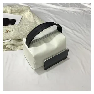 Detailed view of a white minimalist handbag with black woven handle next to a smartphone