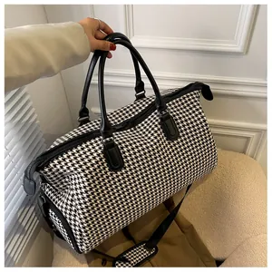 Dettaglio della capiente borsa da viaggio pied-de-poule con manici in pelle e tracolla moda