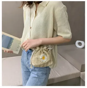 Detail of straw woven bucket bag featuring daisy appliques and white drawstring closure
