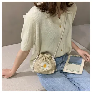 Detail of hand-woven straw bucket bag featuring a white daisy and drawstring closure