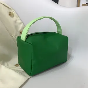 Minimalist green handbag with woven handle and zipper closure shown on a white chair
