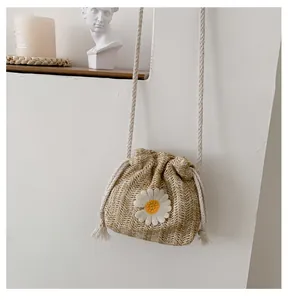 Detail of straw woven bucket bag featuring delicate daisy embroidery and rope drawstring