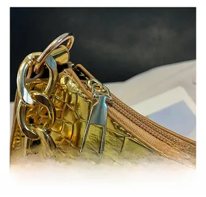 Detail showing smooth gold metal zipper and chunky chain on crocodile texture handbag