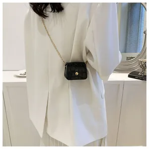 Detail view of a black crocodile pattern micro bag with gold chain on a white suit