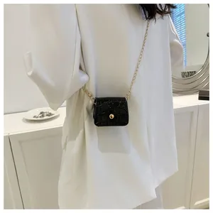 Detail of black croc-embossed mini bag featuring a gold chain strap on a model