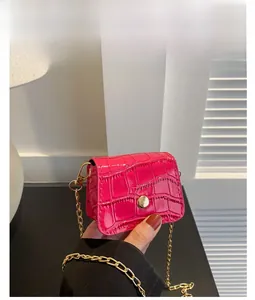 Detail of rose red mini square bag with crocodile pattern and golden chain strap