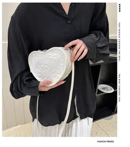 Close-up of white heart-shaped crossbody bag featuring embossed floral clover patterns