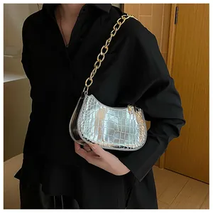Macro detail of silver crocodile pattern texture and gold chain strap on small hobo bag