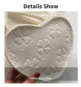 Detail view of heart-shaped white bag featuring clover embossing and gold hardware