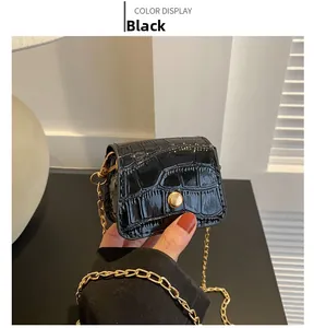 Close-up of a mini black crossbody bag with crocodile texture and gold chain strap