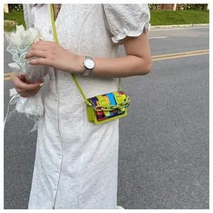 Mini multi-color patchwork shoulder bag with green chain and strap on a white dress