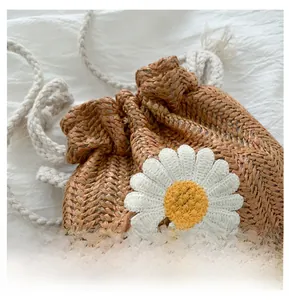 Close-up of woven straw bucket bag with white daisy flower detail and drawstring closure