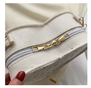 Detailed close-up of smooth gold-tone dual zippers on a creamy heart-shaped felt bag