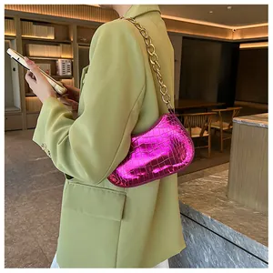 Detail of bright pink crocodile-embossed underarm bag with thick gold chain shoulder strap