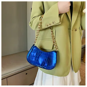 Detail of bright blue crocodile pattern underarm bag with thick gold metal chain strap