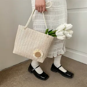 Straw tote bag with sunflower decor and white rope handles held by a model