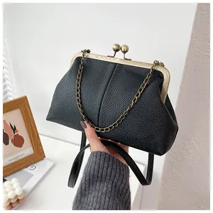 Detail of black lychee texture shell bag with bronze kiss-lock closure and metal chain
