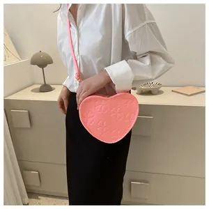Detail of pink heart-shaped crossbody bag with embossed clover patterns on a model