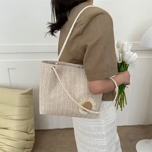 Detail of a beige woven straw tote bag featuring white floral accents and cord handles
