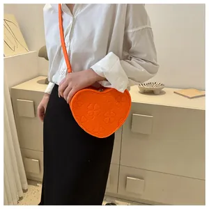 Detail of bright orange heart-shaped crossbody bag with embossed clover patterns