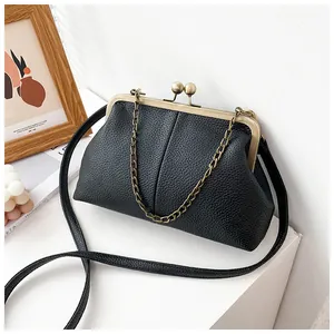Detail of black lychee-textured shell bag with bronze kiss-lock and chain strap