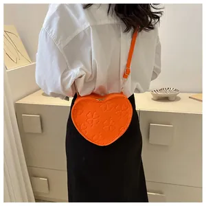 Detail of heart-shaped orange crossbody bag with embossed clover pattern worn on model