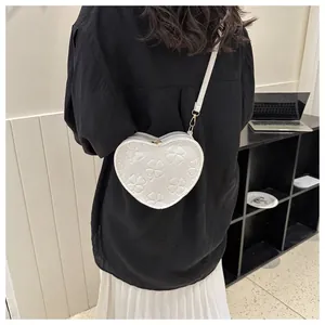 Detail view of heart-shaped white crossbody bag with embossed clover patterns and gold hooks