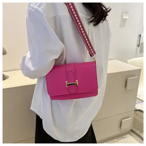 Détail d'un sac bandoulière en cuir rose avec large sangle tissée porté par un modèle