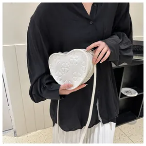 Detail of white heart-shaped crossbody bag with clover embossing and gold metal clips