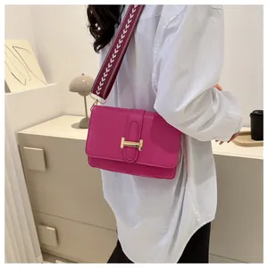 Gros plan d'un sac bandoulière fuchsia avec une boucle métallique dorée en forme de H
