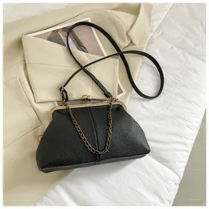 Detailed view of black litchi pattern kiss-lock bag with metal chain on white fabric
