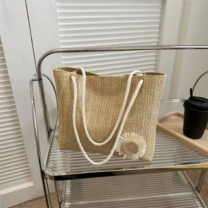Straw woven tote bag with white cotton rope handles and a small daisy floral accent