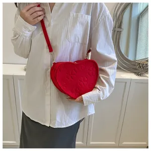 Detail of red heart-shaped shoulder bag with embossed clover pattern and gold metal hooks