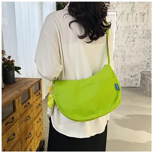 Détail du sac croissant en toile verte avec étiquette bleue et pendentif fleur jaune