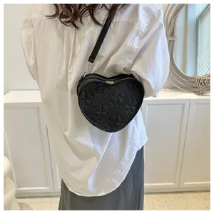Detailed view of black heart-shaped bag with embossed clover patterns and long strap