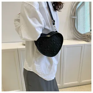 Detail showing black heart-shaped crossbody bag with clover embossing and gold zipper