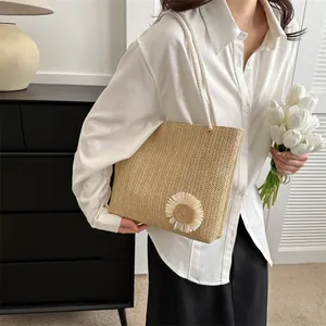 Large woven straw tote bag with daisy detail and rope handles shown on a model