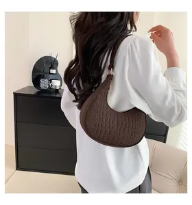 Close-up of a dark brown crocodile-embossed crescent bag with golden buckle on model