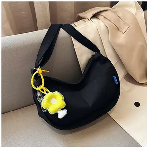 Détail du sac croissant en toile noire avec breloque tournesol sur un canapé gris