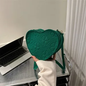 Detail view of heart-shaped forest green felt crossbody bag with embossed clover pattern