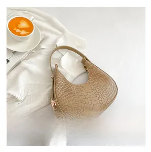 Beige crocodile embossed half-moon shoulder bag styled with a coffee and magazine