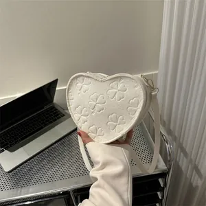 Detail of white heart-shaped bag with embossed clover patterns and golden metal hardware
