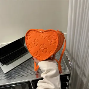 Detail of orange heart-shaped crossbody bag featuring embossed four-leaf clover patterns