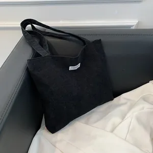 Detail of black corduroy tote bag showing soft ribbed texture and fashion logo patch