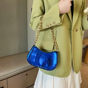 Blue crocodile pattern hobo bag with gold chain strap shown on a green suit outfit