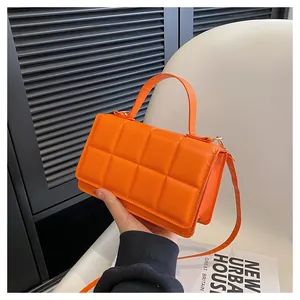 Détails de la texture matelassée orange et des finitions dorées du petit sac à main carré